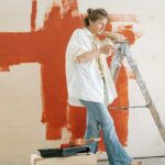 woman in white shirt and blue denim jeans standing beside red wall